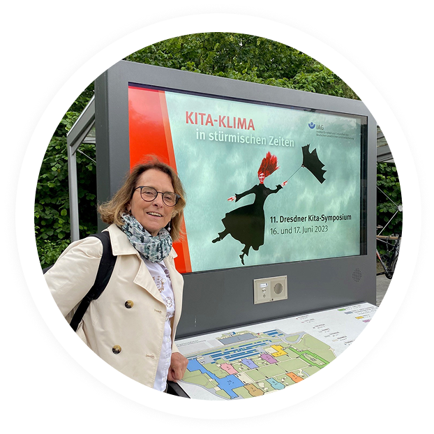 Heidrun Schudak steht vor dem Veranstaltungsbanner „Kita Klima in stürmischen Zeiten“ beim 11. Dresdner Kita Symposium 2023